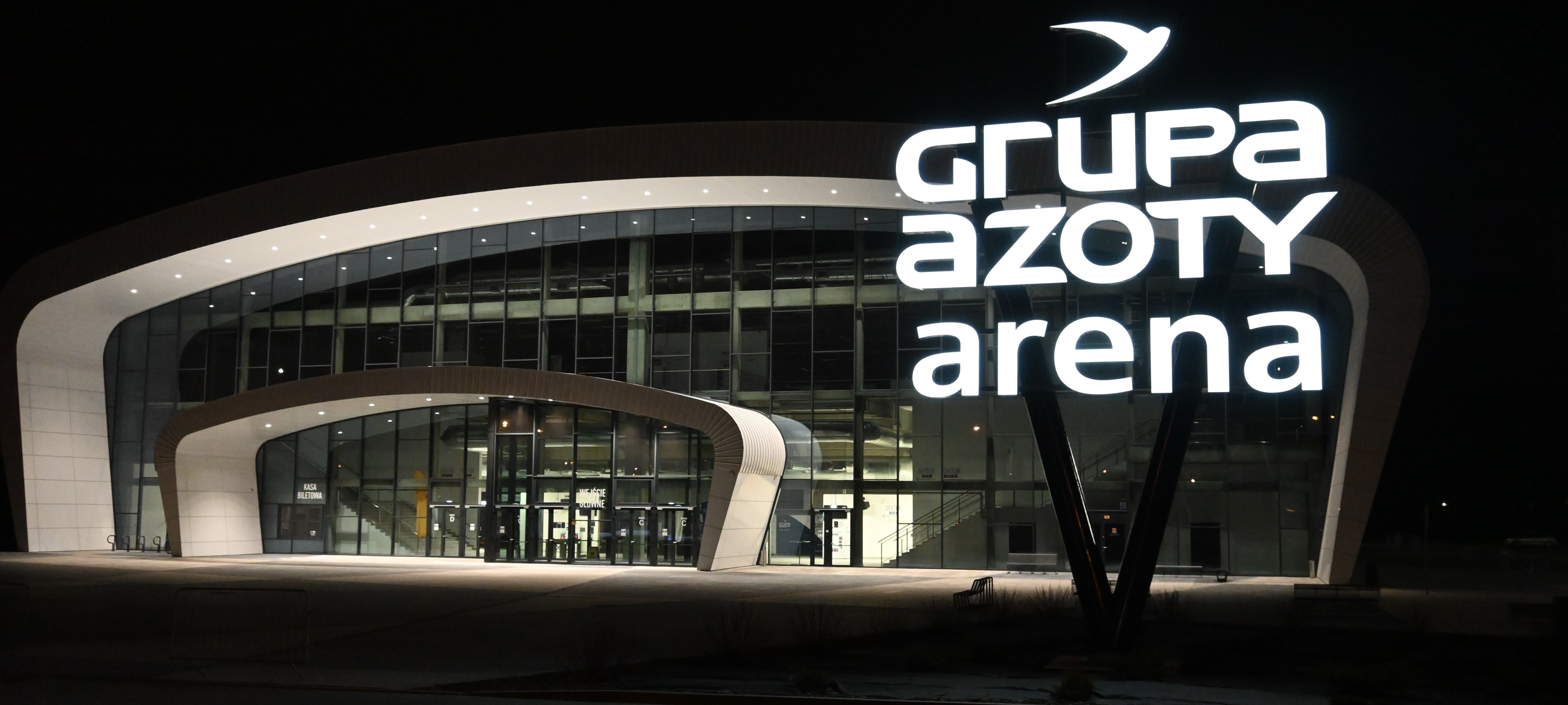Pylon świetlny z napisem Grupa Azoty Arena. Na drugim planie znajduje się hala sportowa Grupa Azoty Arena.