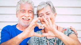 Dwoje uśmiechniętych seniorów składających dłonie w kształt serca